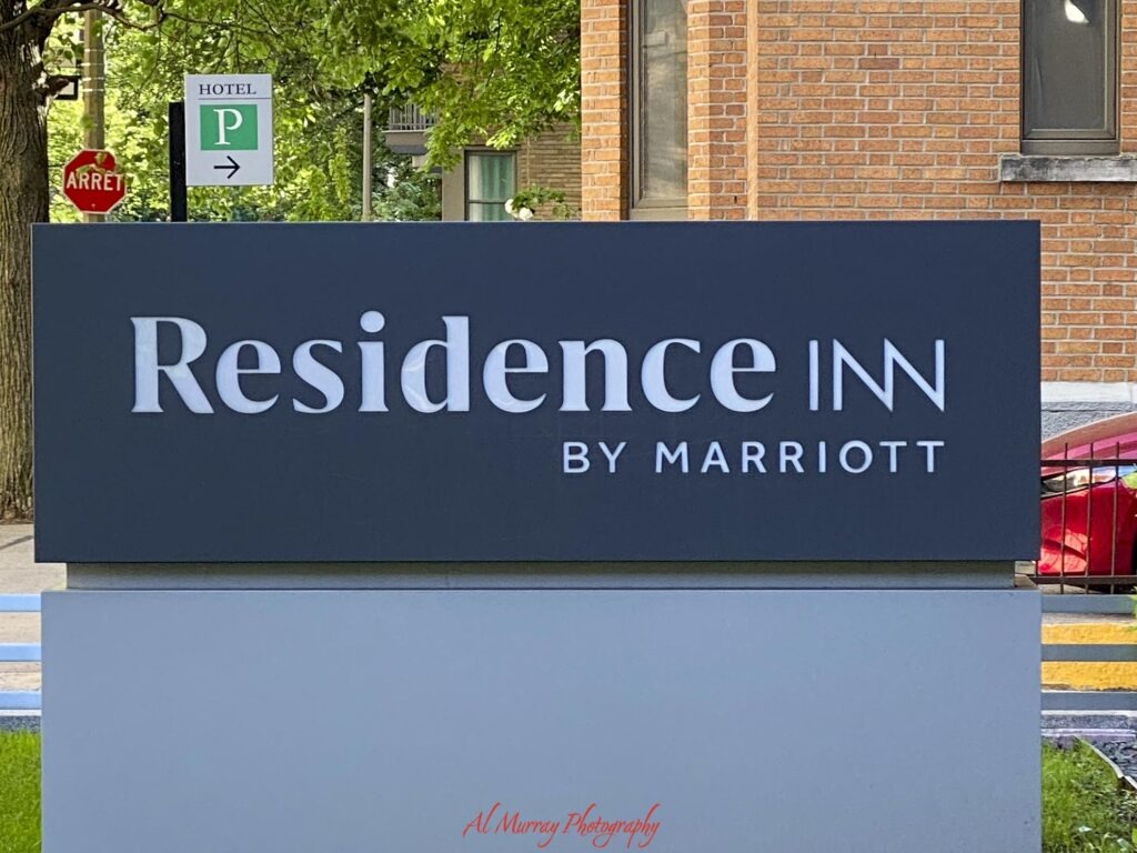 A large roadside hotel sign reads "Residence Inn by Marriott" with a brick building and leafy trees behind it. Nearby signs read "HOTEL" "P" and "ARRET" and the clearly marked parking is a practical detail to consider when deciding how to choose a hotel in Montreal. "Al Murray Photography".