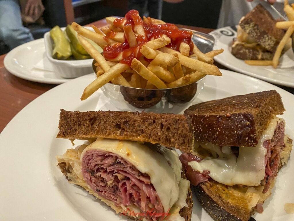 Montreal deli meal with a thick smoked meat sandwich on dark rye bread topped with melted cheese and served with French fries covered in ketchup and pickles. Easy access to casual restaurants like this can be useful when choosing a Montreal hotel near the Metro. "Al Murray Photography".