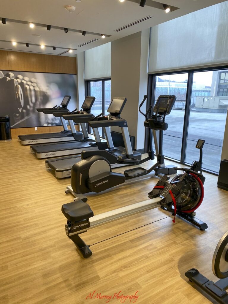 Modern hotel fitness room with treadmills elliptical machines and a rowing machine beside large windows. A gym like this can be a useful amenity when choosing a Montreal hotel near the Metro. "Life Fitness". "Al Murray Photography".