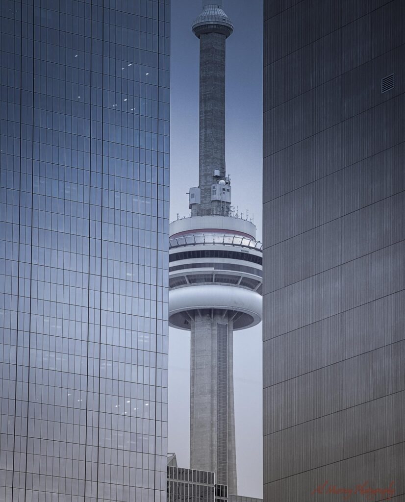 where to stay in Toronto as a solo traveller The CN Tower rises between two modern downtown skyscrapers under an overcast sky.
