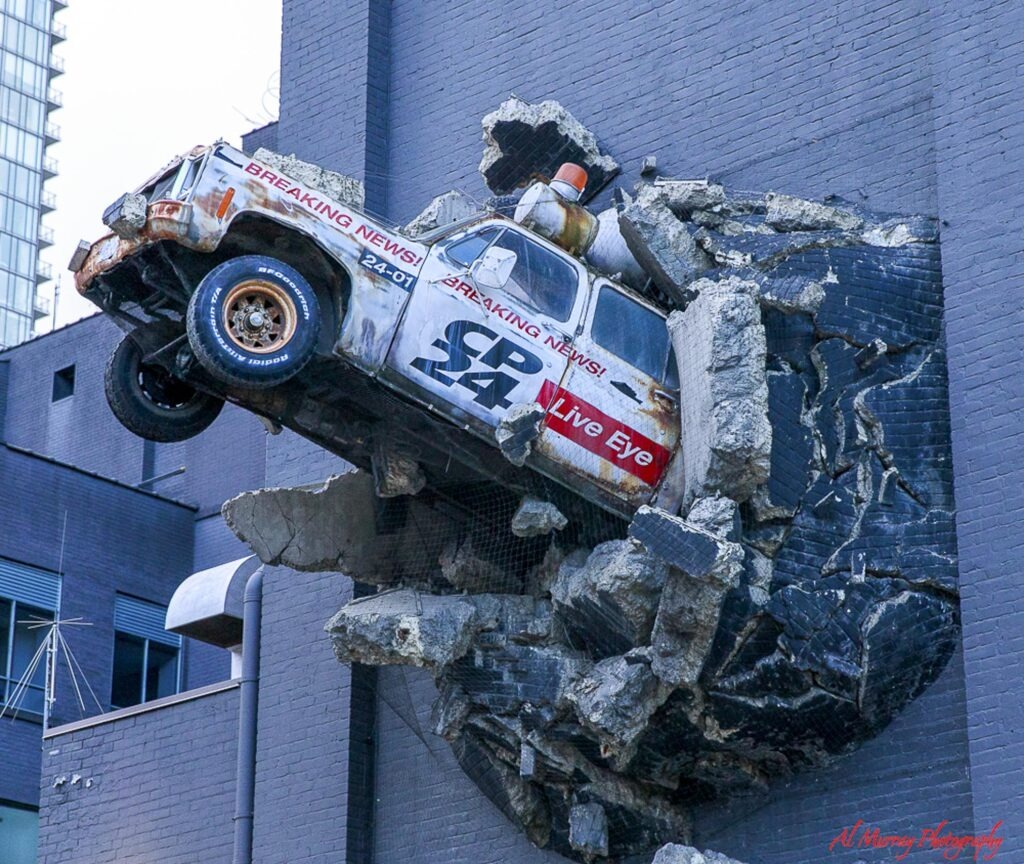 where to stay in Toronto as a solo traveller A weathered news truck appears to burst through a dark brick wall as part of a dramatic urban art installation.