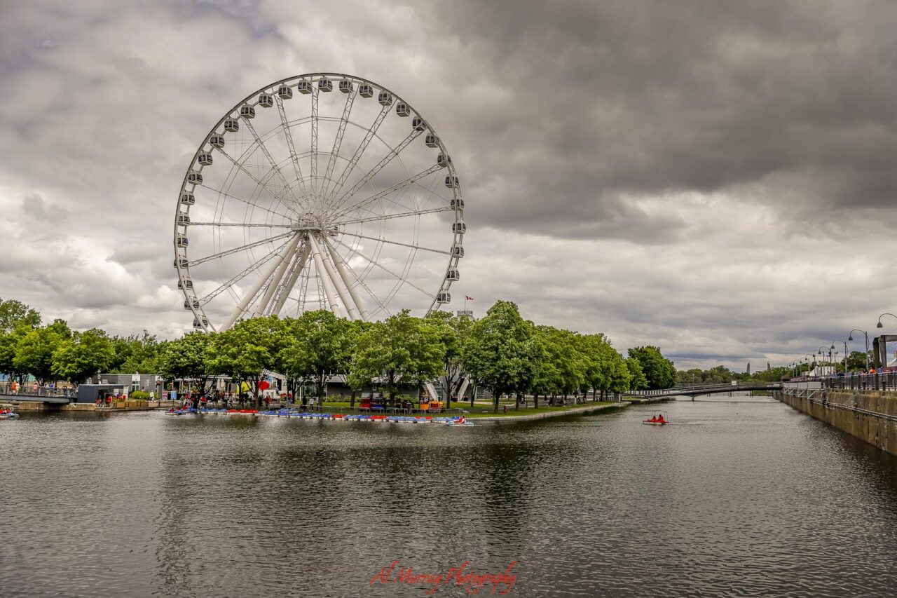 A large white Ferris wheel rises above the waterfront in Montreal beneath dramatic gray clouds. The riverside scene gives travelers searching for deals on hotels in Montreal a look at one of the city’s popular waterfront areas.