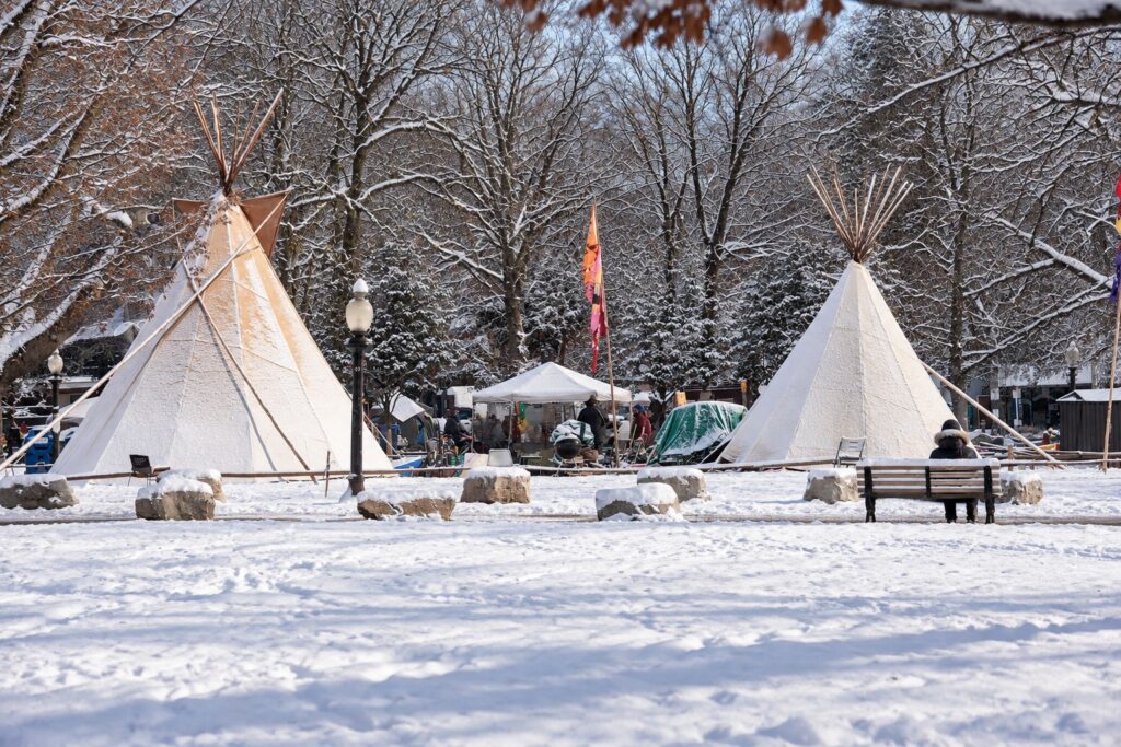 things to do in Toronto indoors Two large teepees stand in a snow covered Toronto park surrounded by bare trees and fresh winter snow. The snowy gathering space highlights an outdoor option among things to do in Toronto when it snows.