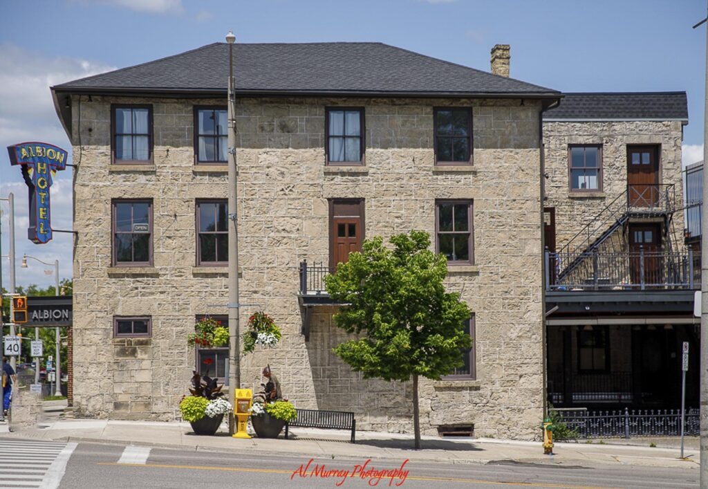 The historic stone Albion Hotel stands on a downtown Guelph street with a colorful vertical sign reading "ALBION HOTEL". The landmark adds local character to a day trip to Guelph from Toronto.