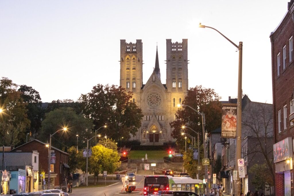 The Basilica of Our Lady Immaculate glows above downtown Guelph at dusk with streetlights and traffic leading toward its twin towers. The landmark is a striking sight to see after traveling to Guelph from Toronto.