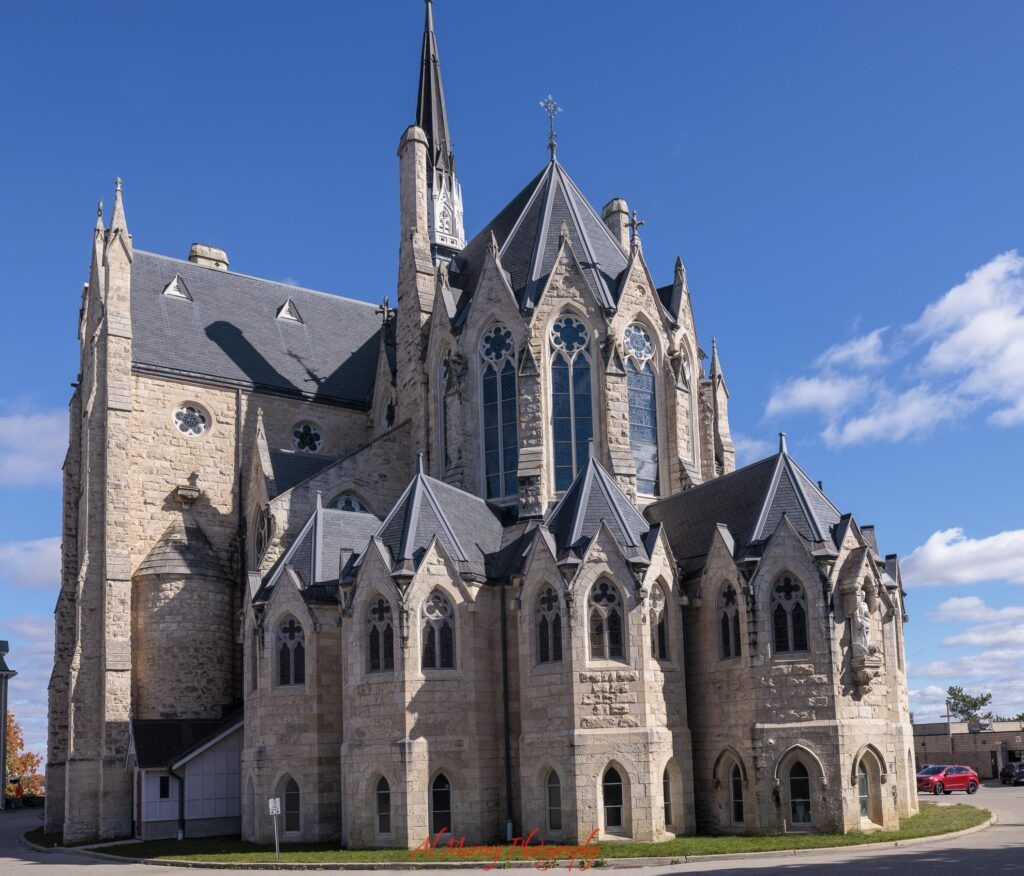 The Basilica of Our Lady Immaculate in Guelph rises against a bright blue sky with pointed spires and detailed Gothic stonework. This historic church is one of the architectural landmarks to see when looking for things to do in Guelph. The photo is marked "Al Murray Photography".