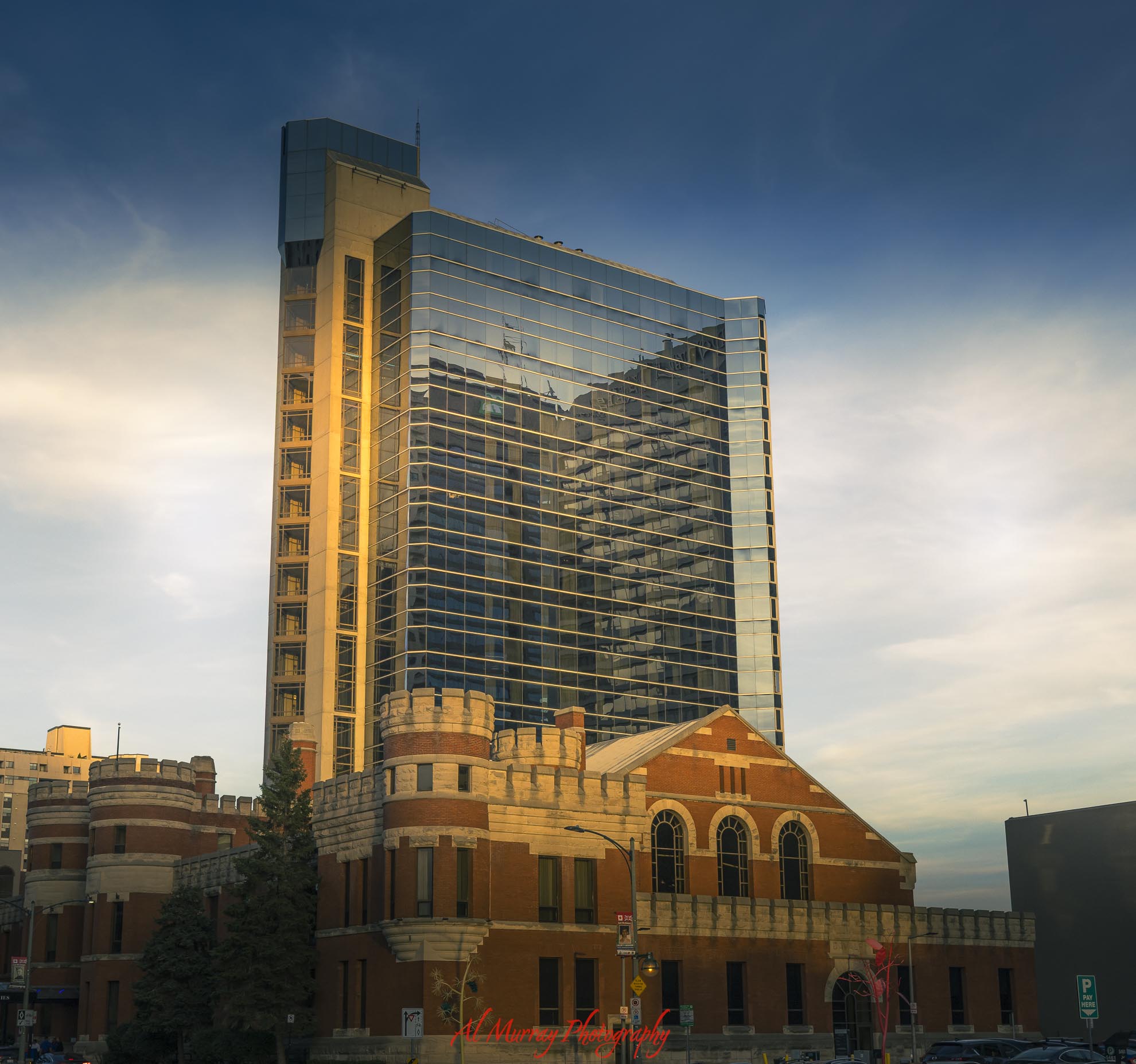 A historic red brick building with castle like stone towers stands beneath a tall modern glass high rise in downtown London Ontario at golden hour. The contrast between old and new architecture adds visual interest for anyone wondering if London Ontario is worth visiting.