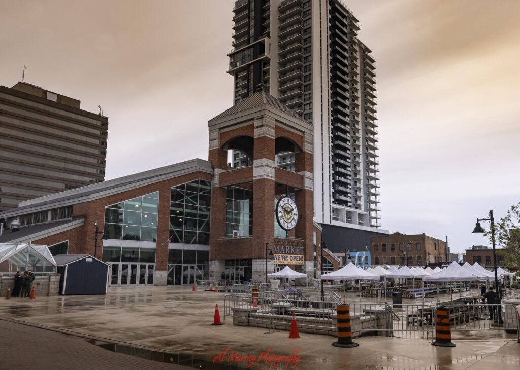 Covent Garden Market in downtown London Ontario stands beside a plaza with white market tents and tall modern buildings rising behind it. The market is a central food and shopping stop to explore during a weekend in London Ontario.