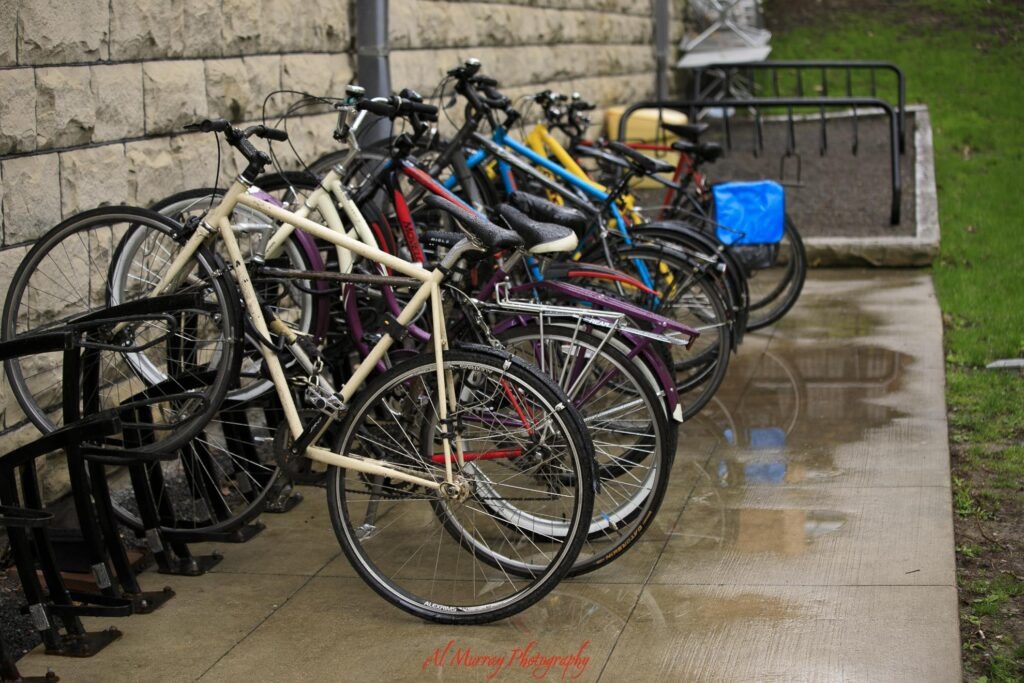 things to do in Toronto indoors Several bicycles are parked beside a stone building on rain soaked pavement with puddles reflecting the bike racks. The wet conditions add context for Toronto rainy day activities and getting around the city in rainy weather.